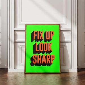 Puede incluir: Un cuadro enmarcado con las palabras "FIX UP LOOK SHARP" en naranja, con letras en 3D sobre un fondo verde brillante. El marco de madera añade un toque clásico al diseño moderno. La obra de arte se exhibe en una pared blanca.