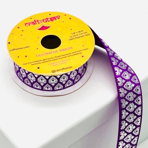 May include: A roll of purple satin ribbon with a silver patterned design. The ribbon is 7/8 inches wide and 30 feet long. The label on the spool says "Decorative Ribbon" and "craftutsav.com".