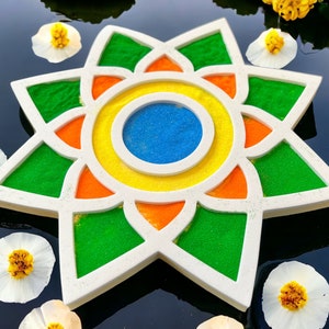 May include: A white star-shaped tray with a colorful mandala design. The mandala features green, orange, yellow, and blue sand.