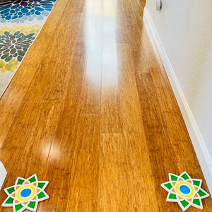 May include: Two colorful, circular, paper floor decorations with a starburst design. The decorations are on a light brown hardwood floor.