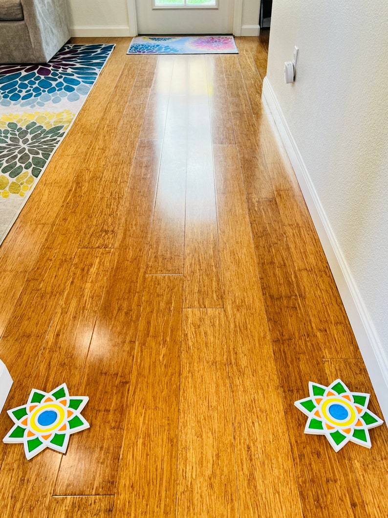 May include: Two colorful, circular, paper floor decorations with a starburst design. The decorations are on a light brown hardwood floor.