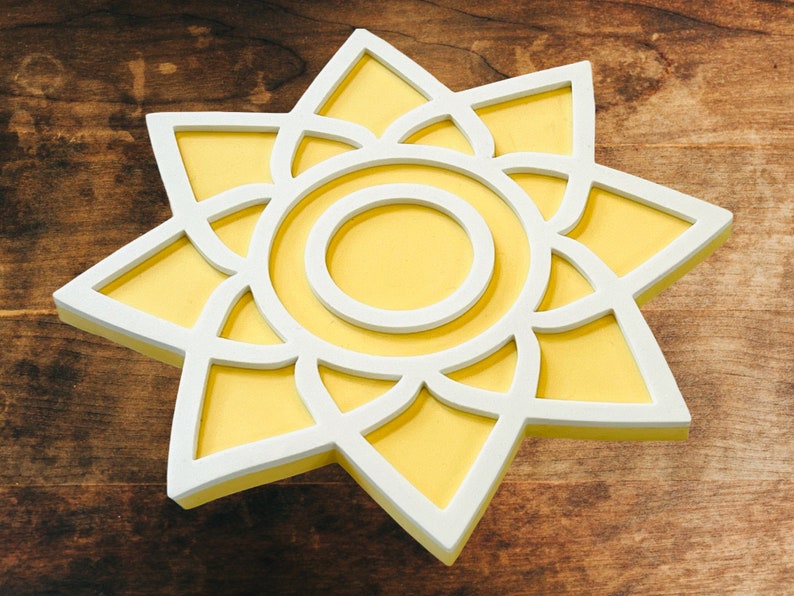 May include: A white and yellow sun-shaped wall decor with a geometric design. The sun has a white outline and a yellow center.