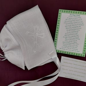 May include: White linen baby bonnet with an embroidered cross design and satin ribbon ties. Includes a green card with a poem and instructions for use. A traditional baptism or christening accessory.