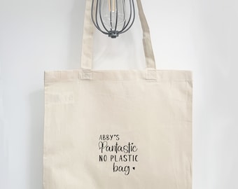 May include: A white canvas tote bag with black text that reads "Abby's Fantastic No Plastic Bag" with a heart symbol.