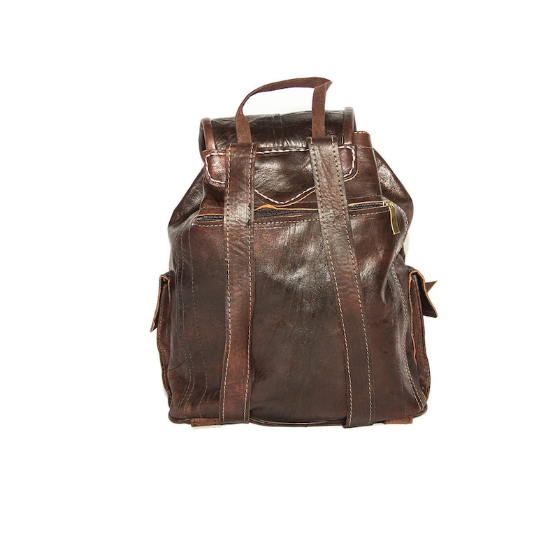 May include: A brown leather backpack with adjustable straps and multiple pockets. The backpack has a worn, vintage look.