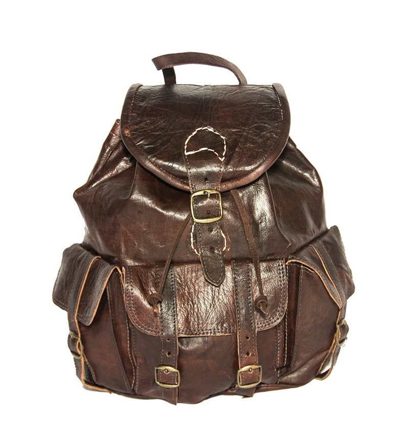 May include: A brown leather backpack with multiple pockets and buckles. The backpack has a flap with a buckle closure and a drawstring closure.