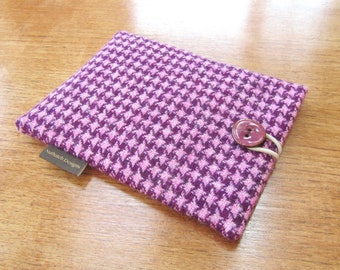May include: A rectangular, houndstooth-patterned case in shades of purple and pink. A large, round button secures the case with an elastic loop. The label reads "Nuthatch Designs".