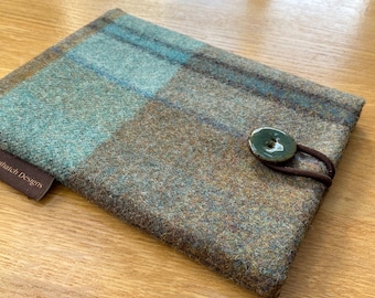 May include: A rectangular, plaid-patterned case in shades of teal, brown, and gray. The case features a dark green button closure with a brown elastic loop. The label reads "thatch Designs".