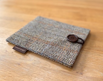 May include: A square, tweed case with a brown button closure. The case features a herringbone pattern in shades of brown, gray, and orange. A small brown tag with the text "Nuthatch Designs" is attached to the case.
