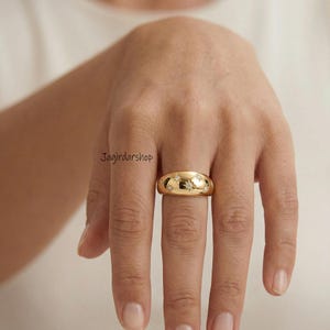 May include: A gold-colored ring with a domed shape, adorned with small, sparkling star-shaped embellishments. The ring is worn on a finger, showcasing its polished surface and intricate design. The ring is a piece of jewelry.
