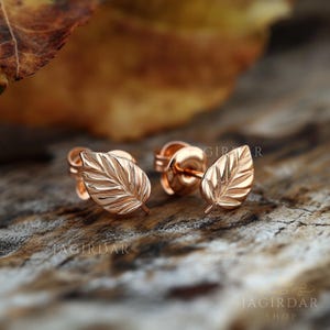May include: A pair of rose gold leaf stud earrings. The earrings are small and delicate, with a detailed leaf design.