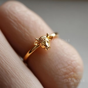 Könnte beinhalten: Ein goldener Ring mit einem detaillierten Stierkopf-Design. Der Ring wird an einem Finger getragen.