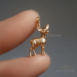 Puede incluir: Colgante de ciervo dorado. El ciervo está de pie con la cabeza girada hacia un lado. El colgante es pequeño y delicado, perfecto para añadir un toque de fantasía a un collar o una pulsera.
