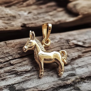 May include: A polished gold-toned metal pendant shaped like a donkey in profile, featuring a smooth, reflective surface and a small integrated bail at the top for attachment to a chain. The design includes detailed ears, a mane, and a curled tail.