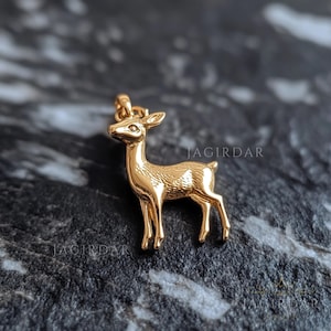 Puede incluir: Un colgante de ciervo de tono dorado. El ciervo está de pie con la cabeza alta y la cola levantada. El colgante es una representación detallada y realista de un ciervo.