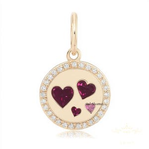 May include: A gold pendant with a round charm featuring three hearts. The charm is surrounded by a halo of small diamonds. The hearts are red and pink.