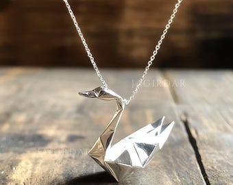 Może przedstawiać: Srebrny naszyjnik z zawieszką w kształcie origami łabędzia. Łabędź jest popularnym symbolem pokoju i wdzięku.
