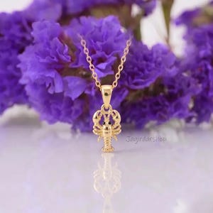 May include: A gold-toned necklace featuring a lobster-shaped pendant with small black accents for the eyes. The pendant hangs from a delicate gold-toned chain. The text Jagirdarshop is visible in the lower right area of the image.