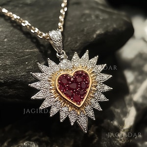 Puede incluir: Un collar de plata y oro con un colgante en forma de corazón de rubí rojo rodeado de una estrella de diamantes. El colgante está en una cadena de plata.