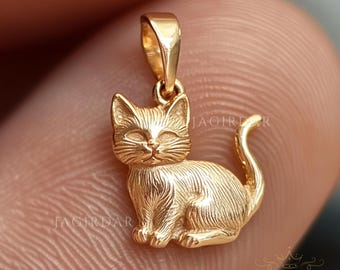 May include: A gold-coloured pendant in the shape of a sitting cat. The cat has a detailed, textured surface and a small loop at the top for attaching to a chain.