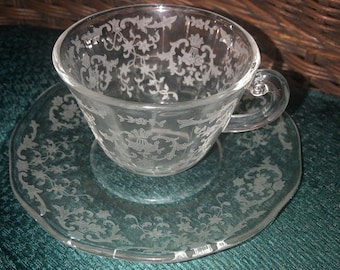 May include: A clear glass teacup and saucer set with a delicate floral pattern. The set is made of clear glass and has a vintage look.