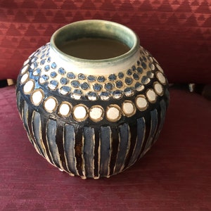 May include: A ceramic vase with a blue, white, and brown geometric pattern. The vase has a round body and a wide opening.