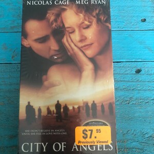 May include: A VHS tape of the movie City of Angels starring Nicolas Cage and Meg Ryan. The cover features a close-up of Cage and Ryan looking at each other. The price tag reads $7.95. The text on the cover reads "She didn't believe in angels until she fell in love with one."