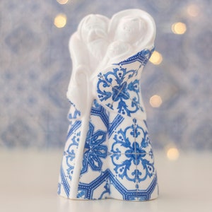 May include: White ceramic figurine of the Holy Family, with blue and white patterned clothing reminiscent of Portuguese tiles. The figures are depicted in a loving embrace.