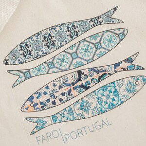 May include: A white tote bag with a blue and white design of four fish. The fish are patterned with blue and white tiles. The text "FARO PORTUGAL" is printed on the bag.