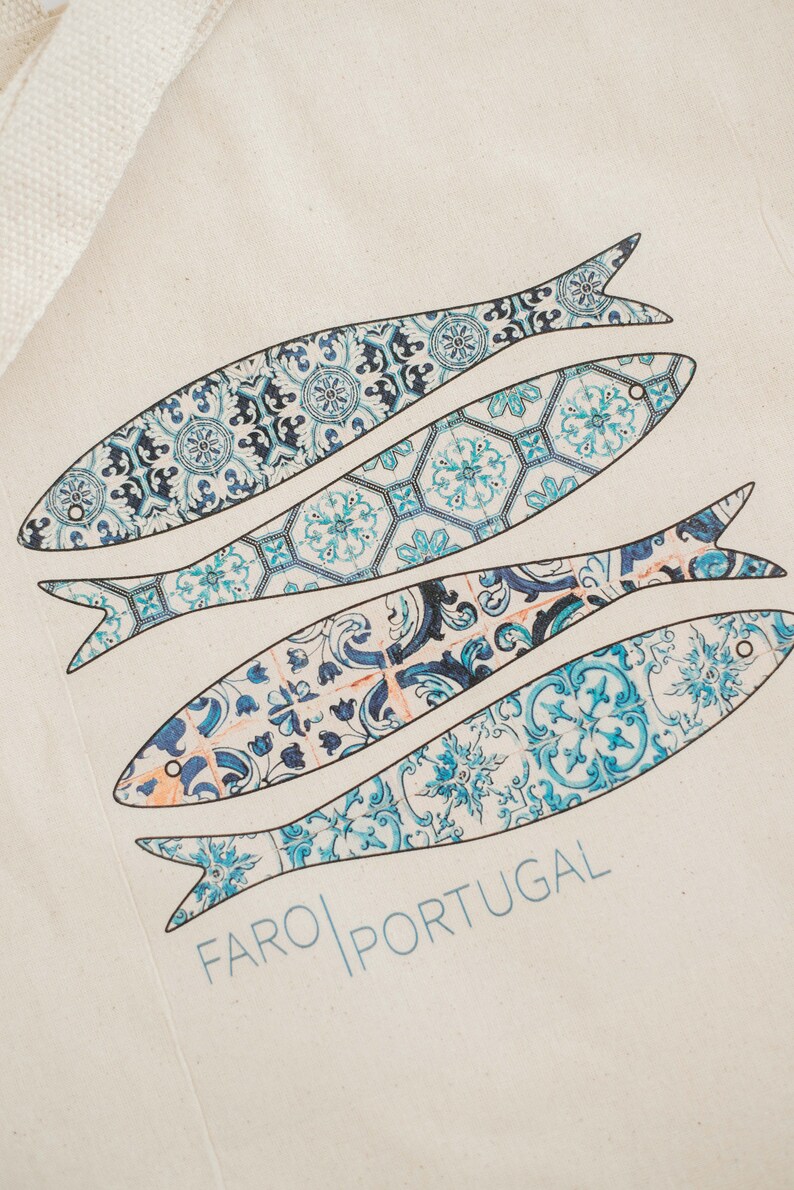 May include: A white tote bag with a blue and white design of four fish. The fish are patterned with blue and white tiles. The text "FARO PORTUGAL" is printed on the bag.