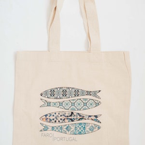 May include: A white canvas tote bag with blue and white patterned fish designs and the text "FARO PORTUGAL".