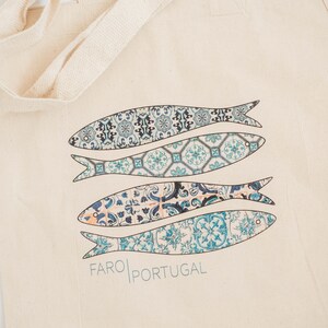 May include: A beige canvas tote bag with blue and white patterned fish and the text "FARO PORTUGAL" printed on the front.