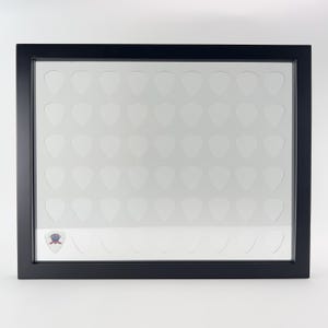 Könnte beinhalten: Schwarzer Rahmen mit einer klaren Glasfront. Der Rahmen hat 64 einzelne Fächer in Form von Gitarrenplektrum. Die Fächer sind leer.
