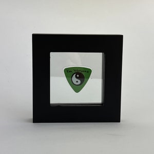 May include: A black framed display case with a green guitar pick inside. The pick has a yin yang symbol and the text "Ken Yokoyama" written on it.