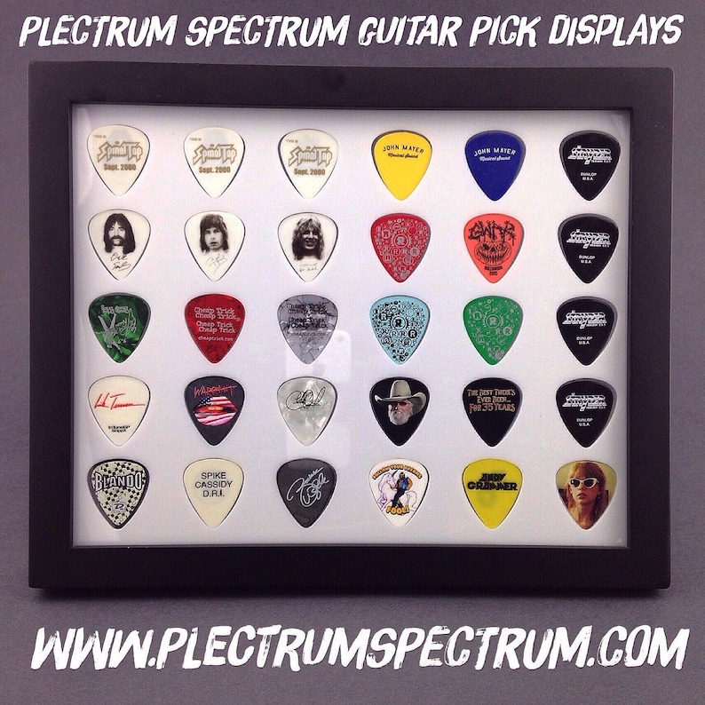 May include: A black framed display case with a white background showcasing a collection of guitar picks. The picks feature various band logos, names, and designs, including "S2000", "John Mayer", "The Best There's Ever Been", "Blando", and "Spike Cassidy DRI".