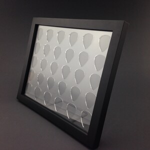 May include: Black framed display case with clear acrylic inserts for holding guitar picks. The case has 36 individual slots for storing picks.