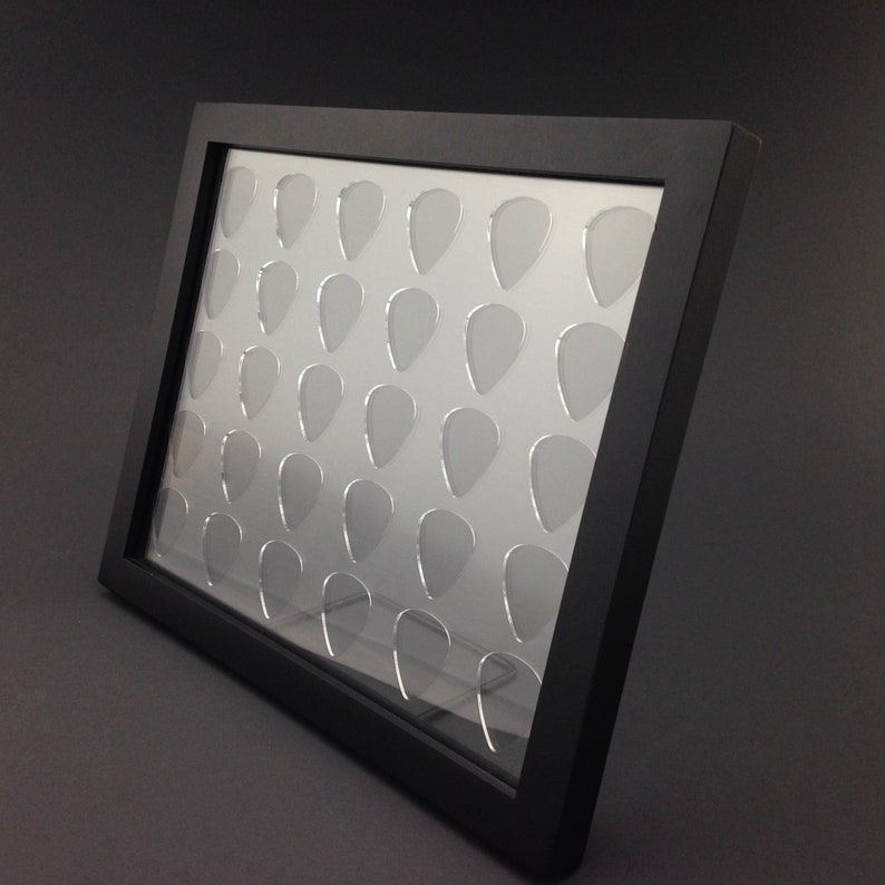 May include: Black framed display case with clear acrylic inserts for holding guitar picks. The case has 36 individual slots for storing picks.