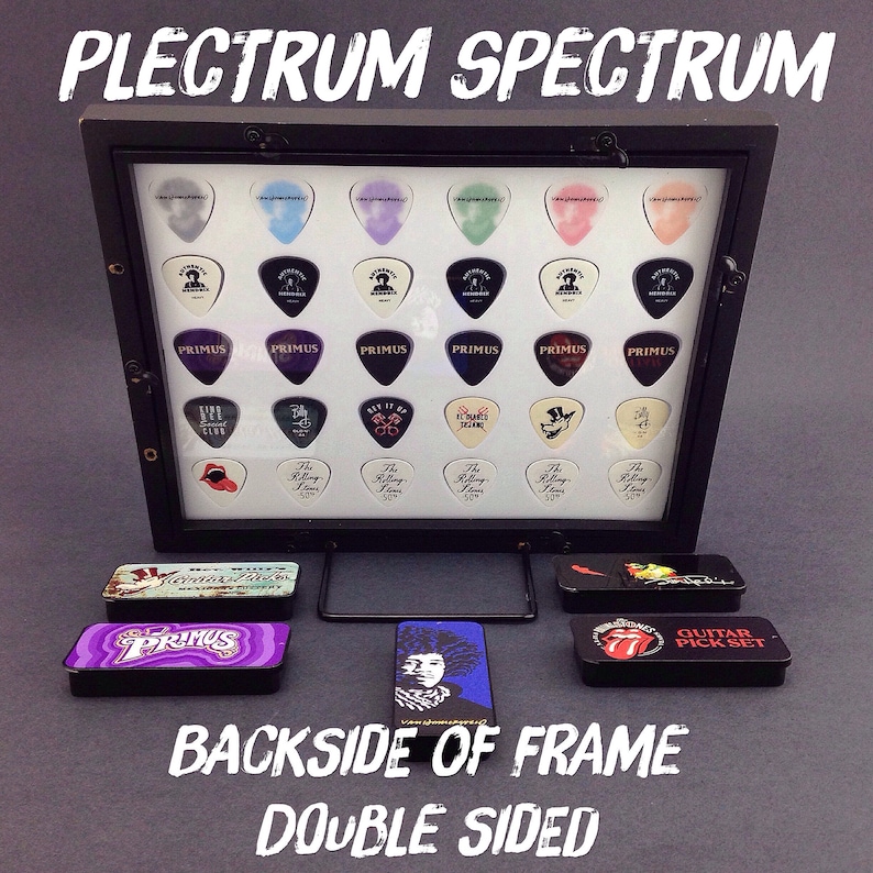 May include: A black frame with a clear acrylic front displaying a collection of guitar picks. The picks feature various band logos, including "Primus", "The Rolling Stones", and "KISS". The frame is double-sided and has a black stand.