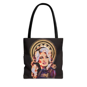 May include: Black tote bag with a portrait of a woman with blonde hair and a gold halo. The bag has black handles and a black background. The portrait is framed by a gold circular design. The artist's signature is at the bottom.