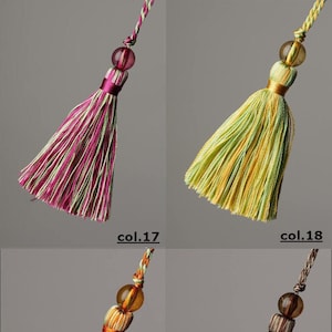 May include: Four different coloured tassels with beads. The tassels are made of a striped fabric and have a fringe at the bottom. The beads are clear and have a slight amber colour. The tassels are labelled with the numbers 17, 18, 19, and 20.