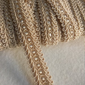 Puede incluir: Borde beige con un diseño de cuentas. El borde está hecho de una tela suave y tejida y tiene un aspecto delicado y elegante.