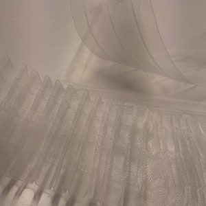 Op de afbeelding: Close-up van witte, transparante stof met een geplooide rand. De stof is gelaagd, waardoor een textuureffect ontstaat. Het materiaal lijkt licht en doorschijnend, geschikt voor knutselen of decoratieve doeleinden.