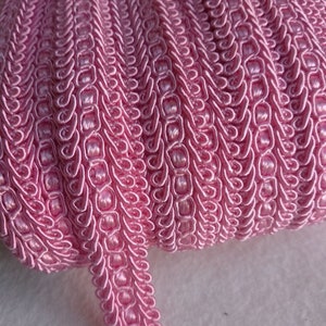 Peut inclure: Un rouleau de garniture décorative rose. La garniture est faite d'un matériau tissé avec un motif répétitif de boucles et de courbes. La couleur est un rose clair et doux, et la garniture semble neuve et inutilisée. Cette garniture convient aux projets de couture et d'artisanat.