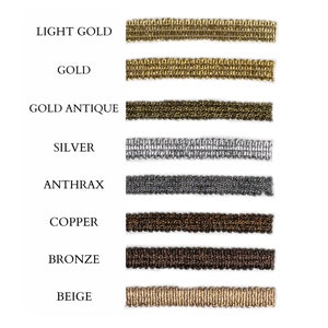 Op de afbeelding: Een close-up van acht verschillende gekleurde trimstalen. De kleuren zijn licht goud, goud, antiek goud, zilver, antraciet, koper, brons en beige.