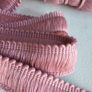 Pode incluir: Franja rosa com franjas e borda festoneada. A franja é feita de tecido macio e tecido com um detalhe de franja.