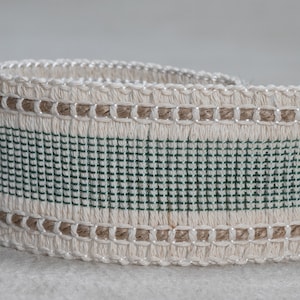 May include: A close-up of a white woven trim with a green stripe and a brown woven edge.