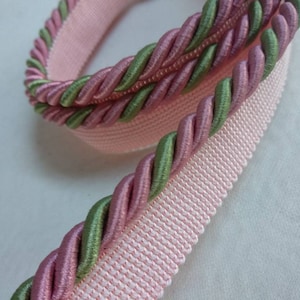 Könnte beinhalten: Rosa und grüner geflochtener Besatz mit einem rosa gewebten Rücken. Der Besatz ist etwa 2,5 cm breit.