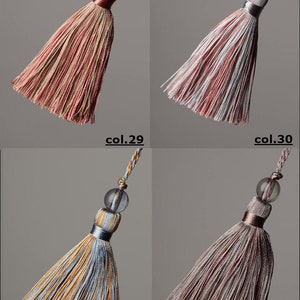 May include: Four different coloured tassels with a clear glass bead at the top. The tassels are made of a striped fabric in shades of pink, white, blue, and brown.