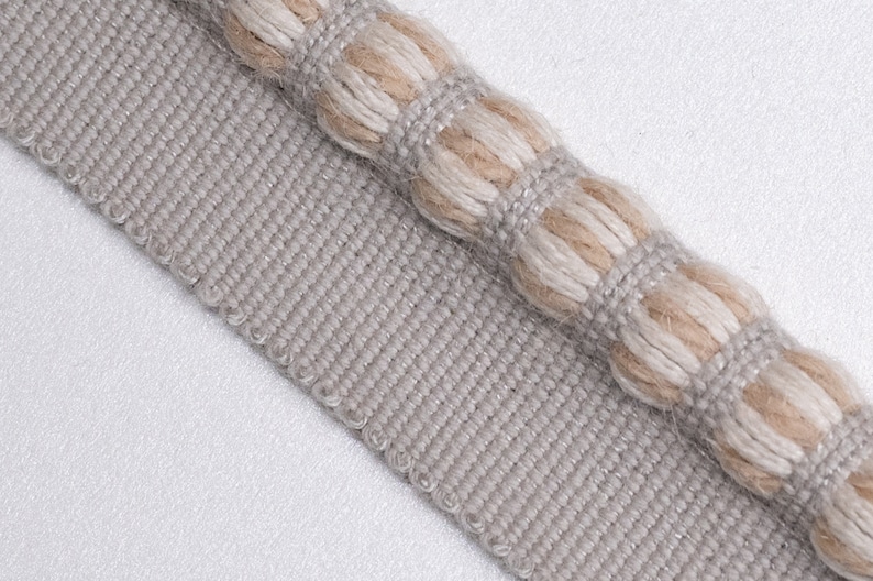 May include: A close-up of a gray and beige trim with a textured, woven design. The trim has a raised, rope-like detail along the edge.