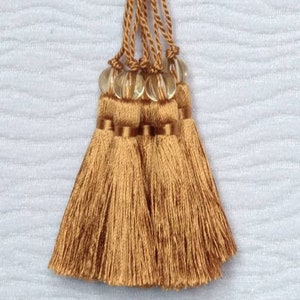 Puede incluir: Un conjunto de cuatro borlas marrones con cuentas de vidrio transparentes. Las borlas están hechas de un material suave y sedoso y tienen aproximadamente 7,6 cm de largo.